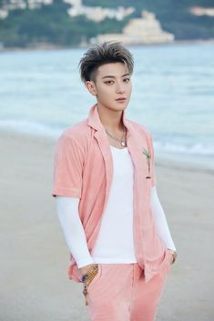 a young man standing on top of a sandy beach next to the ocean with his hands in his pockets