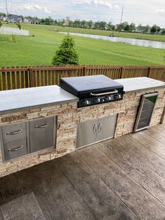 an outdoor bbq with grills and cabinets on a deck overlooking a grassy area