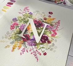 the letter v is painted with watercolor flowers and leaves on it's side