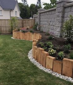 a garden with wooden planters and rocks in the grass next to a brick wall