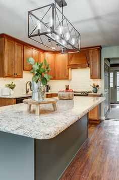 a kitchen with wooden cabinets and marble counter tops, an island in the middle has a potted plant on it