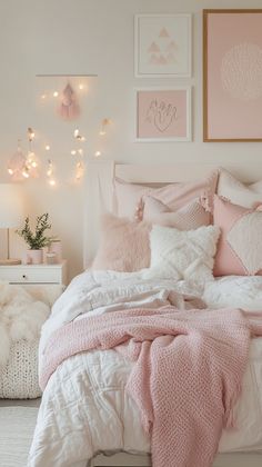 a white bed with pink pillows and blankets on it in a bedroom decorated with lights