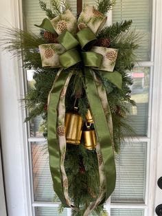 a christmas wreath with two bells hanging from it's side and pine cones on the front door