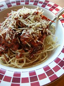 spaghetti with meat sauce and parmesan cheese in a red and white bowl on a checkered plate