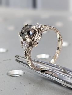 a close up of a ring on top of a pair of tongs with some diamonds in it