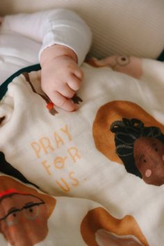 a baby laying on top of a bed covered in a blanket that says pray for us