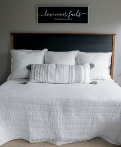 a bed with white linens and pillows in a bedroom next to a framed sign