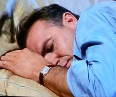 a man sleeping on top of a bed with his arm wrapped around his head and wearing a watch