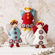 three felt angel ornaments hanging from strings on a white surface with beads and chains around them