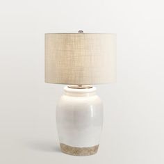 a white table lamp with a beige shade on the base and a light brown drum