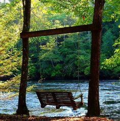 a wooden swing hanging from the side of a river