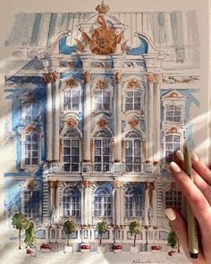 a woman's hand holding a pencil over a drawing of a blue and white building