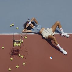 a woman laying on top of a tennis court holding a racquet and tennis balls