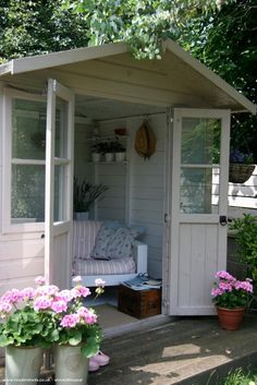 a small white shed with potted plants and flowers in the front porch area next to it