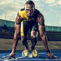 a man in yellow shirt and black shorts standing on a blue track with his legs crossed