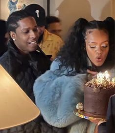 two women look at a chocolate cake with lit candles