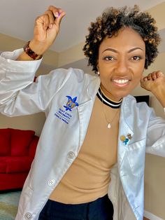 a woman wearing a white lab coat standing in front of a red couch with her hands on her head