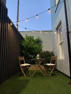 two wooden chairs sitting next to each other on top of a grass covered yard with string lights