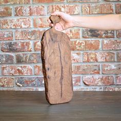 a hand holding a piece of wood in front of a brick wall