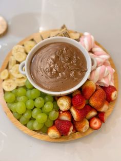 a bowl of chocolate dip surrounded by fruit on a plate