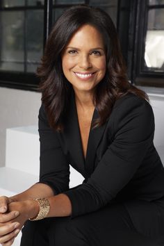 a woman sitting on top of a white bench wearing a black suit and gold bracelet