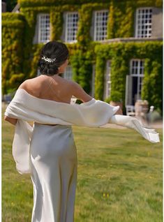 a woman in a long white dress is walking through the grass with her arms outstretched