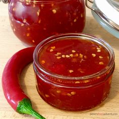 two jars filled with red sauce sitting on top of a wooden table next to a green pepper