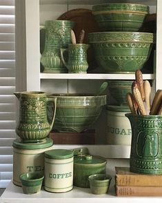 green ceramic dishes and utensils are displayed on the shelf in front of white shutters