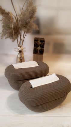 two knitted objects sitting next to a vase with dried plants in it on a table