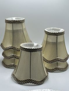 three lampshades sitting next to each other on a white tablecloth covered surface