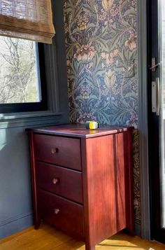 a wooden dresser sitting in front of a window next to a wallpapered wall