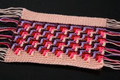 a close up of a knitted piece of cloth on a black surface with pink, purple and red squares