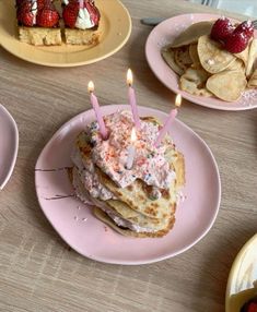 a table topped with pancakes covered in frosting and lit candles next to plates filled with desserts