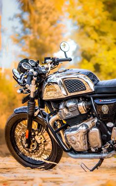 a motorcycle parked on the side of a dirt road in front of trees with yellow leaves