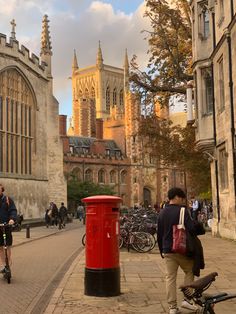 two people riding bikes down a street next to tall buildings and a red post box