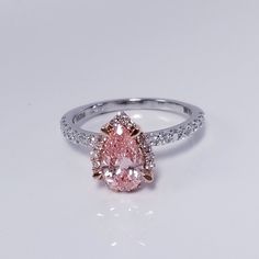 a pink diamond ring with white diamonds around it on a plain surface, set in 18k white gold