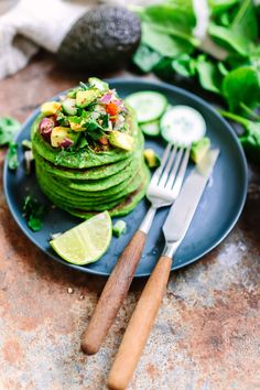 a stack of green pancakes with avocado and other toppings on a plate