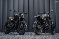 two motorcycles parked next to each other in front of a metal wall with black paint