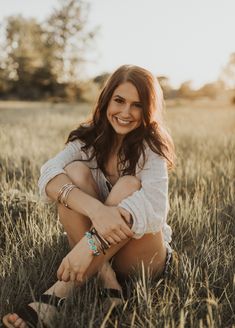 a woman sitting in the middle of a field smiling at the camera with her hands on her knees