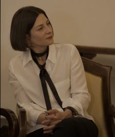 a woman sitting in a chair wearing a white shirt and black tie with her hands crossed