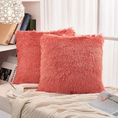 two orange pillows sitting on top of a bed next to a book shelf and lamp