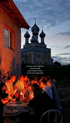 a group of people sitting around a table with food and drinks in front of a church