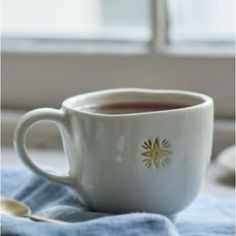 a cup of tea sitting on top of a blue towel next to a spoon and window