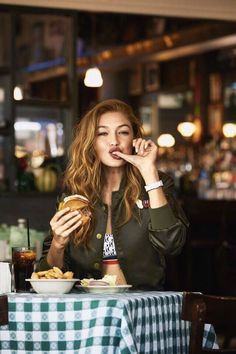 a woman sitting at a table eating food and talking on the phone while holding a hamburger in her hand