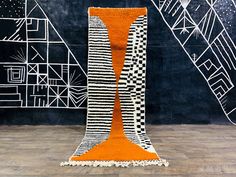 an orange and white rug on the floor in front of a black wall with abstract designs