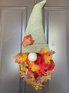 a wreath with an elf's hat hanging from the front door decorated with autumn leaves