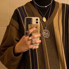 a person holding a cell phone in their hand and wearing jewelry on her neck, standing next to a white tiled wall