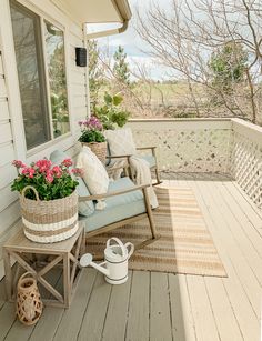 a porch with flowers and plants on the back deck, next to a chair that has a pillow on it