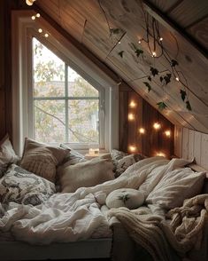 an unmade bed in a loft with lights strung from the ceiling and pillows on it