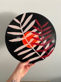 a hand holding up a black and red plate with leaves on the inside, in front of a white wall